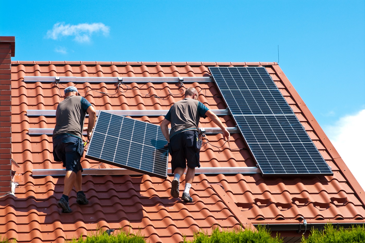 Zwei Solarteure bei der Befestigung einer Photovoltaikanlage auf einem Hausdach.