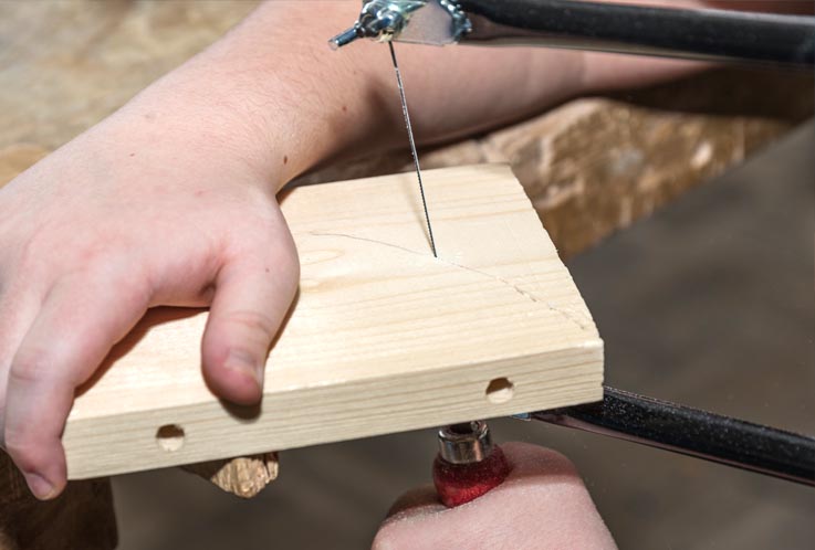 Ein Stück Holz wird mit einer Laubsäge an einer Linie entlang gesägt.