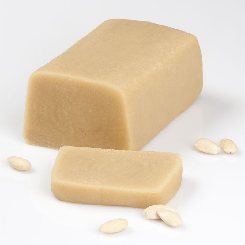 Hellbrauner Marzipan-Block mit einer Scheibe und mehreren geschälten Mandeln auf weißem Hintergrund