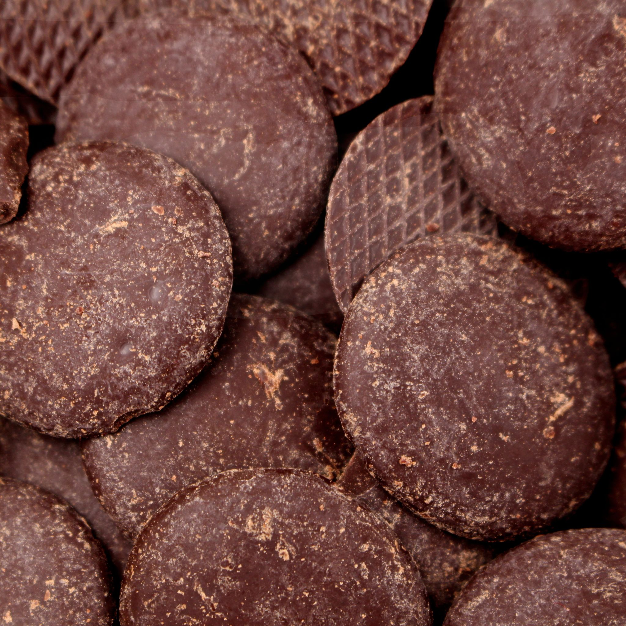 Nahaufnahme runder Zartbitter-Schokoladen-Callets mit leichtem Fettreif und matter Oberfläche