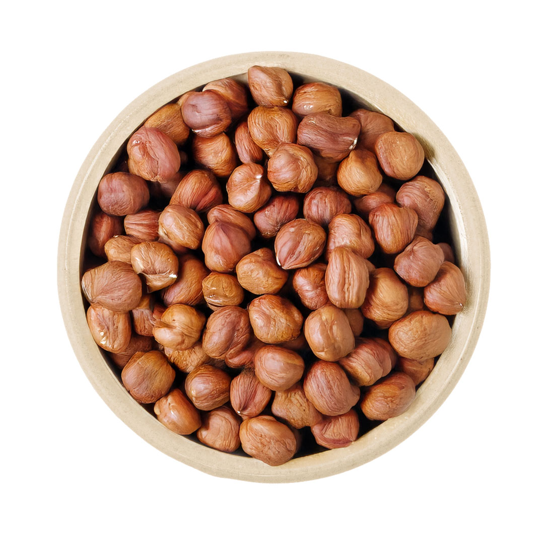 Vogelperspektive auf eine runde Holzschale voller naturbelassener Haselnusskerne mit brauner Haut vor weißem Hintergrund