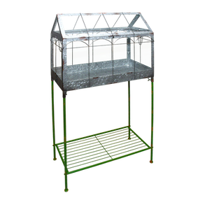 Een vintage-stijl kweekkas van metaal en glas, geplaatst op een groene metalen standaard met een extra plank onderaan.