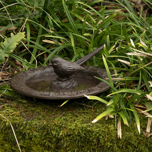 Een gietijzeren zonnewijzer in de vorm van een vogelbad met een vogelfiguur op de rand.