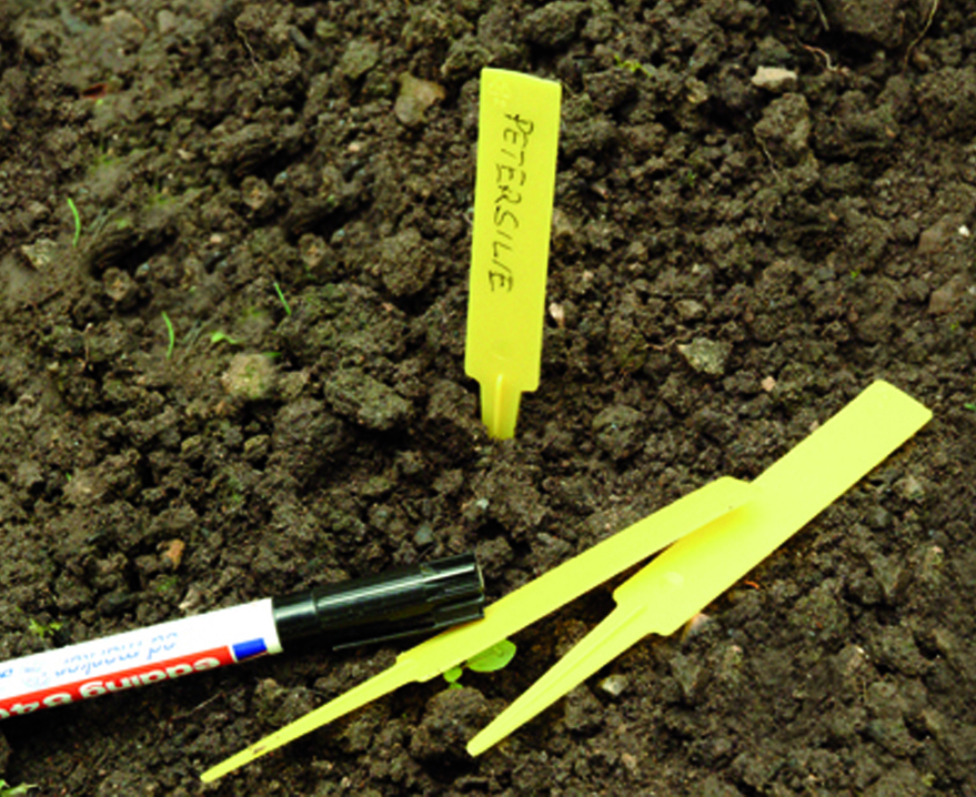 Gele plastic steeketiketten met zwarte marker op aarde, klaar om planten te labelen.