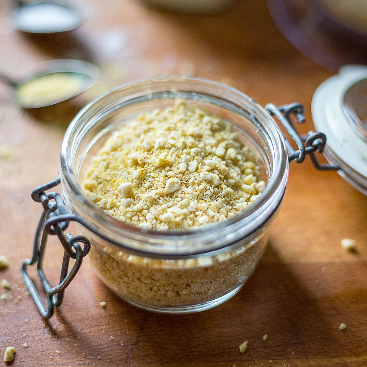 Ein Glas mit veganem Parmesan. Dieses Rezept zeigt dir, wie du im Handumdrehen leckeren, gesunden veganen Parmesan selbst machst, der viele Gerichte perfekt ergänzt!