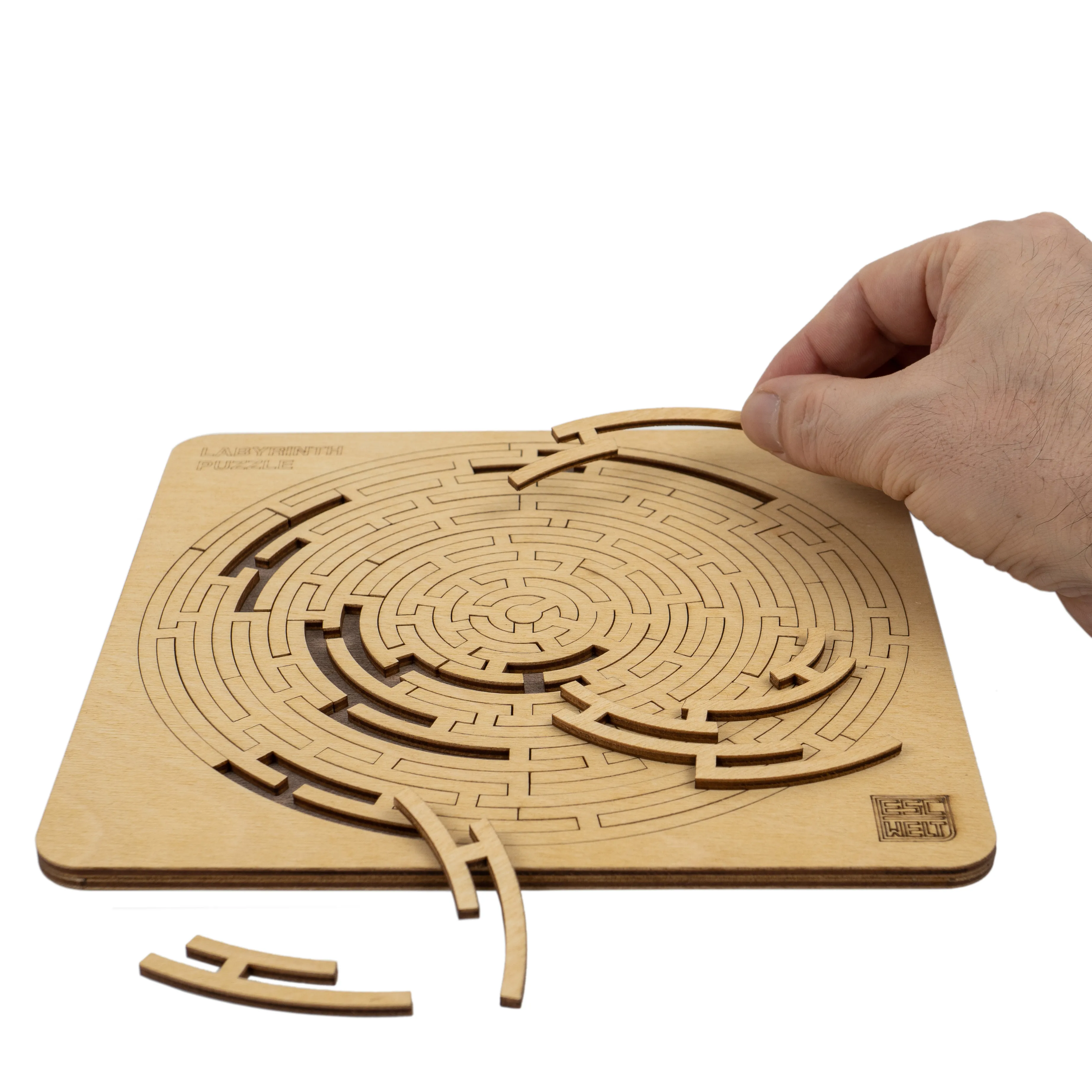 Hand setzt ein Holzteilstück in ein rundes, mehrschichtiges Labyrinth-Puzzle ein.