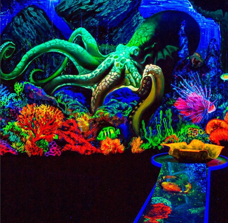 Eine beeindruckende Schwarzlicht-Minigolfbahn mit einem leuchtenden Unterwasser-Motiv. Ein riesiger, grüner Kraken mit leuchtenden Tentakeln ragt aus einem farbenfrohen Korallenriff hervor. Die Szene wird durch bunte Fische, Korallen und ein intensives Sc