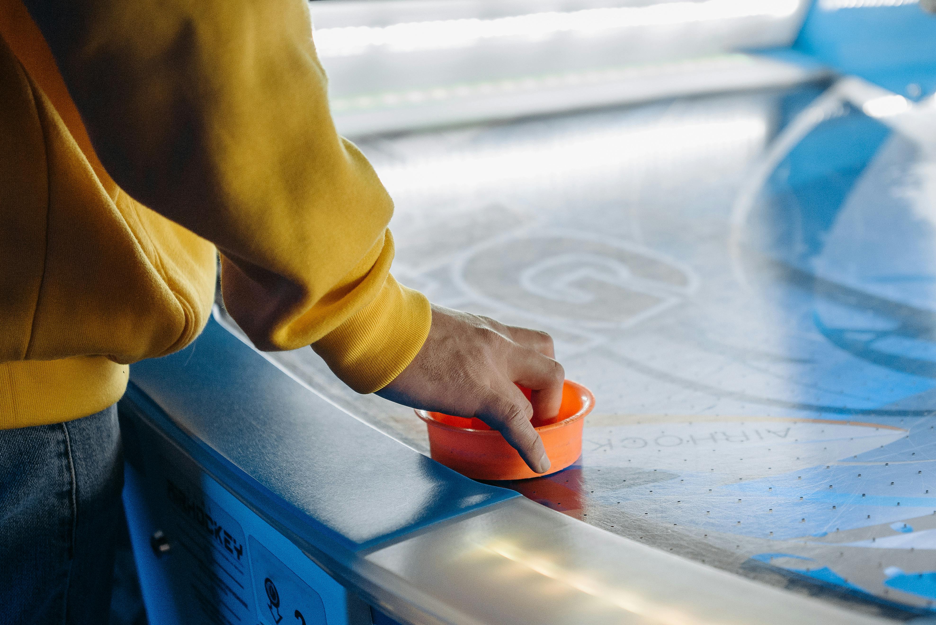 Ein Gast bei LaserStar taucht in ein mitreißendes Airhockey-Spiel ein, wobei er sein Geschick und seine Leidenschaft für das Spiel zeigt. Seine Hände sind geschickt am Schläger, während er den Puck über das Feld bewegt, um sein Ziel zu erreichen. Ein Bild