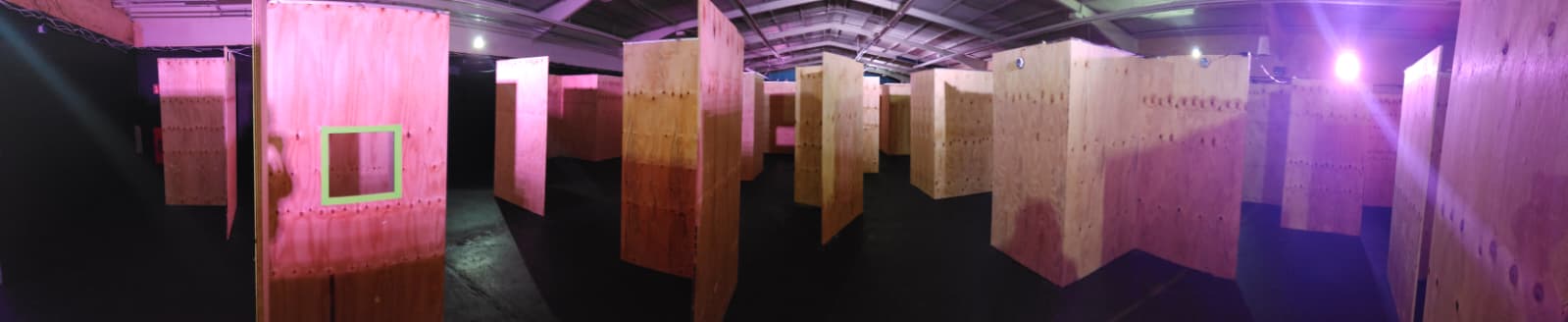 weitwinkelaufnahme der lasertag-arena in oldenburg mit zahlreichen robusten holz-stellwaenden ausgeleuchtet mit neon-und uv-licht