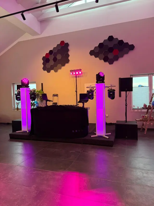 Professionelles DJ-Setup mit Licht- und Tontechnik, beleuchteten Säulen, Moving Heads und Uplighting in einer Hochzeitslocation.