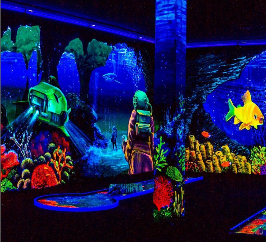 Eine faszinierende Schwarzlicht-Minigolfbahn mit einem tiefseethematisierten Motiv. Ein Taucher in einem alten Taucheranzug beobachtet eine mystische Unterwasserlandschaft. Im Hintergrund sind ein leuchtend grünes U-Boot mit hellen Scheinwerfern, ein groß