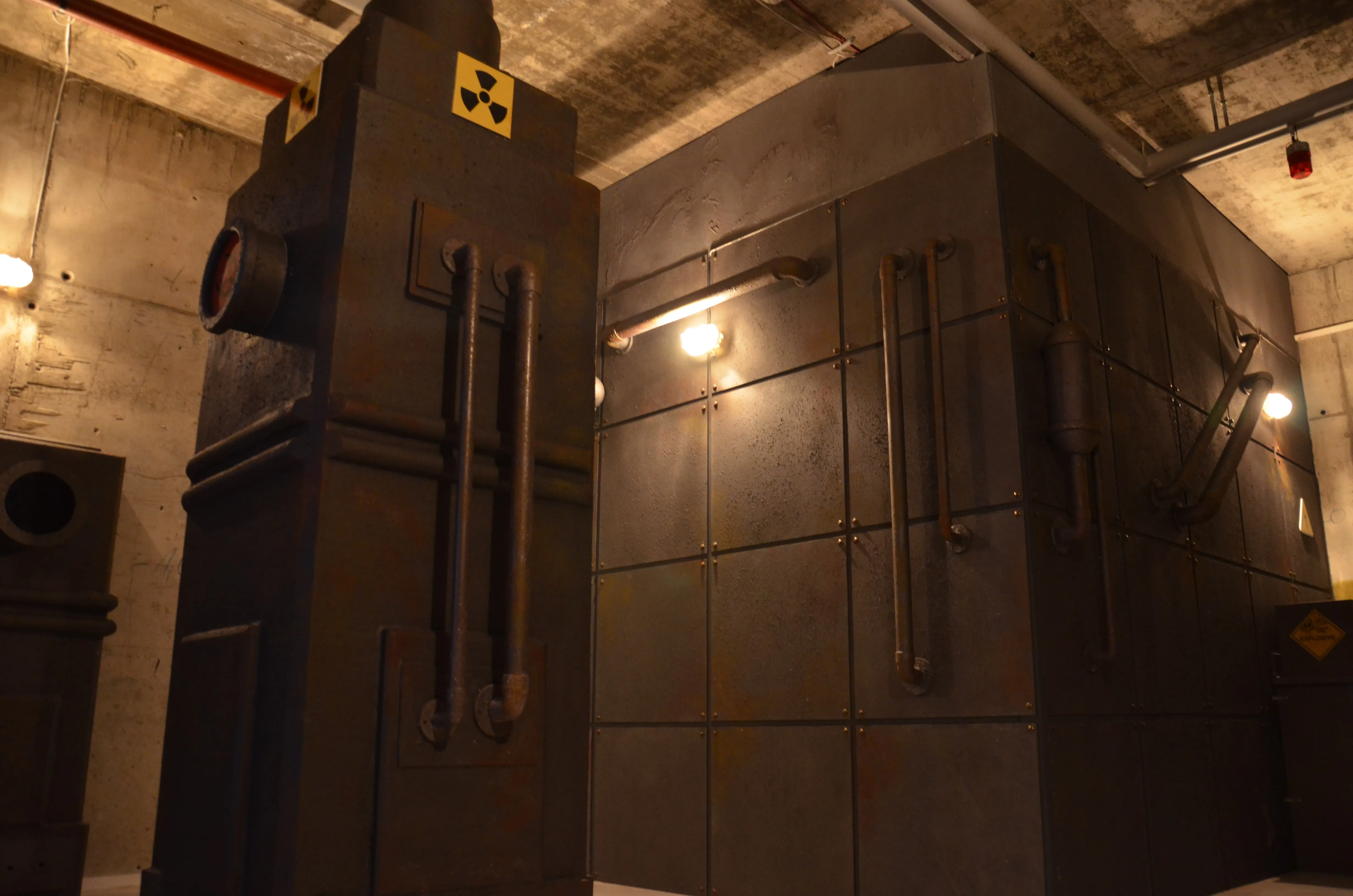 Ein Raum mit industriellem Flair, der an eine Anlage zur Handhabung radioaktiver Materialien erinnert. Zu sehen sind große, dunkle Metallkonstruktionen mit Rohren und einem Warnsymbol für Radioaktivität.