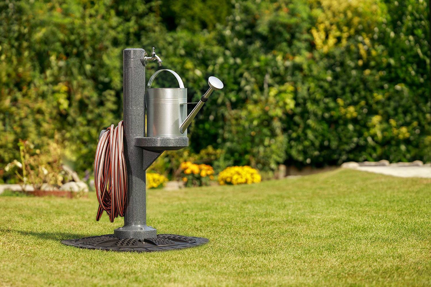 Zapfsäule aus Kunststoff in anthrazit mit Gießkannenablage und Schlauchhalterung aufgestellt im Garten auf dem Zisternendeckel.