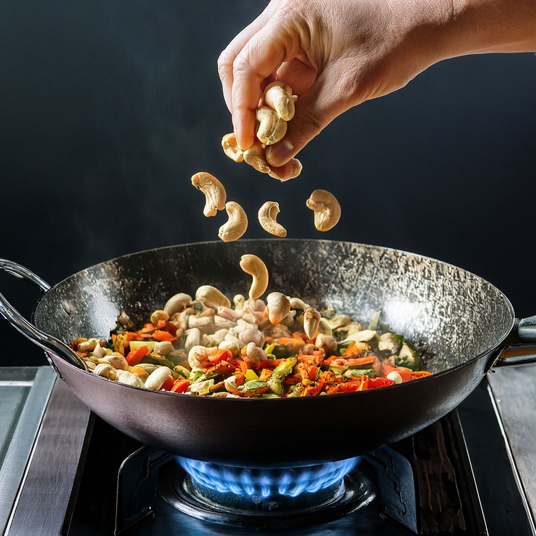 Hand streut Cashewkerne in Wok mit gebratenem Gemüse auf Gasherd