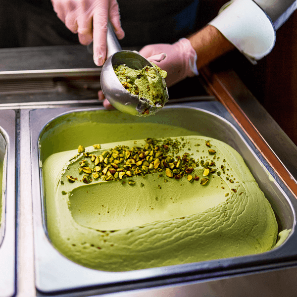 Pistachio gelato with chopped nuts Hand scooping pistachio gelato topped with nuts