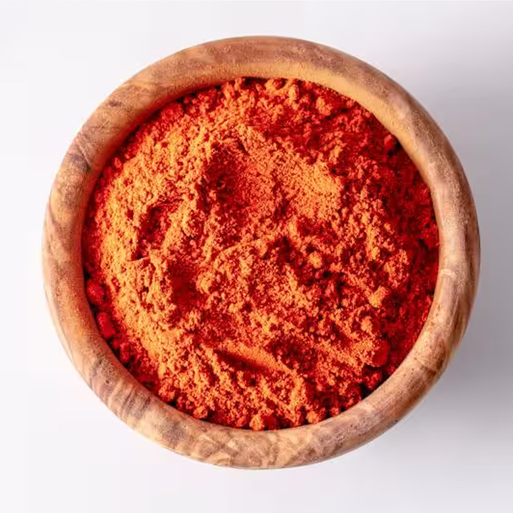 Nahaufnahme: feines rotes Paprikapulver in einer runden Holzschale auf weißem Hintergrund