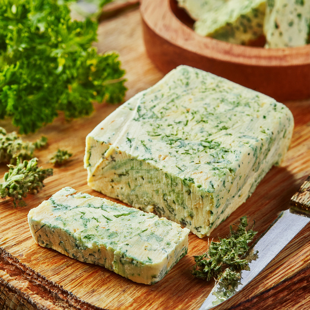 Ein Block frische Kräuterbutter auf einem Holzbrett mit einem Messer und Kräutern