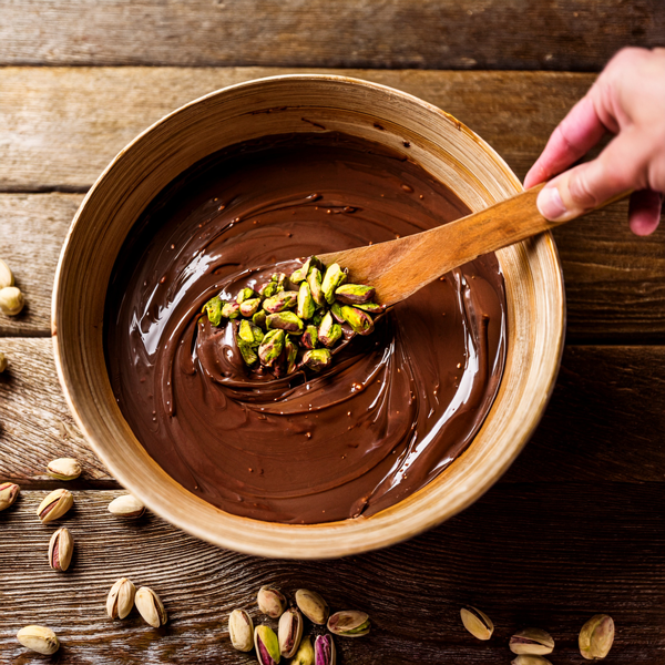 Wooden spoon stirring pistachios in melted chocolate