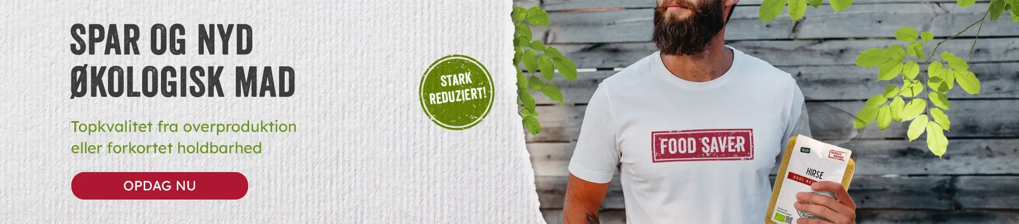 Mand med skæg iført 'Food Saver' T-shirt, der holder en pakke økologisk hirse foran en træbeklædt baggrund med grønt løv.