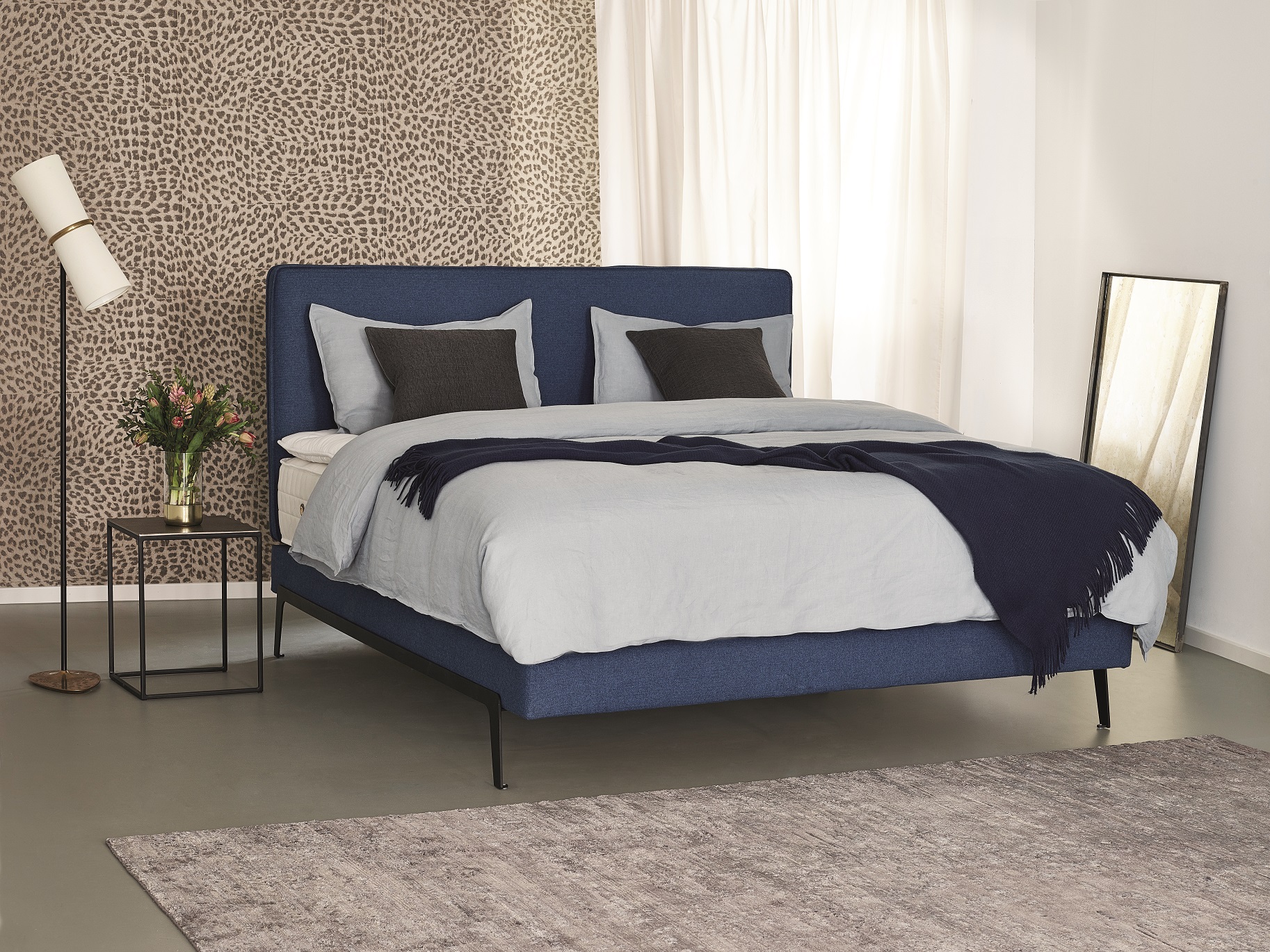 Dunkelblaues Treca Bett mit hellblauer Bettwäsche in einem Zimmer aus hellen Naturtönen