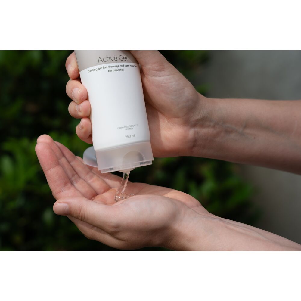 Ein Hand hält eine Tube mit Active Gel, aus der ein gelartiges Produkt in die offene Handfläche fließt. Der Hintergrund zeigt grüne Pflanzen. Die Tube hat folgende Beschriftung: -Cooling gel for massage and sore muscles. No colorants-, -Dermatologisch get