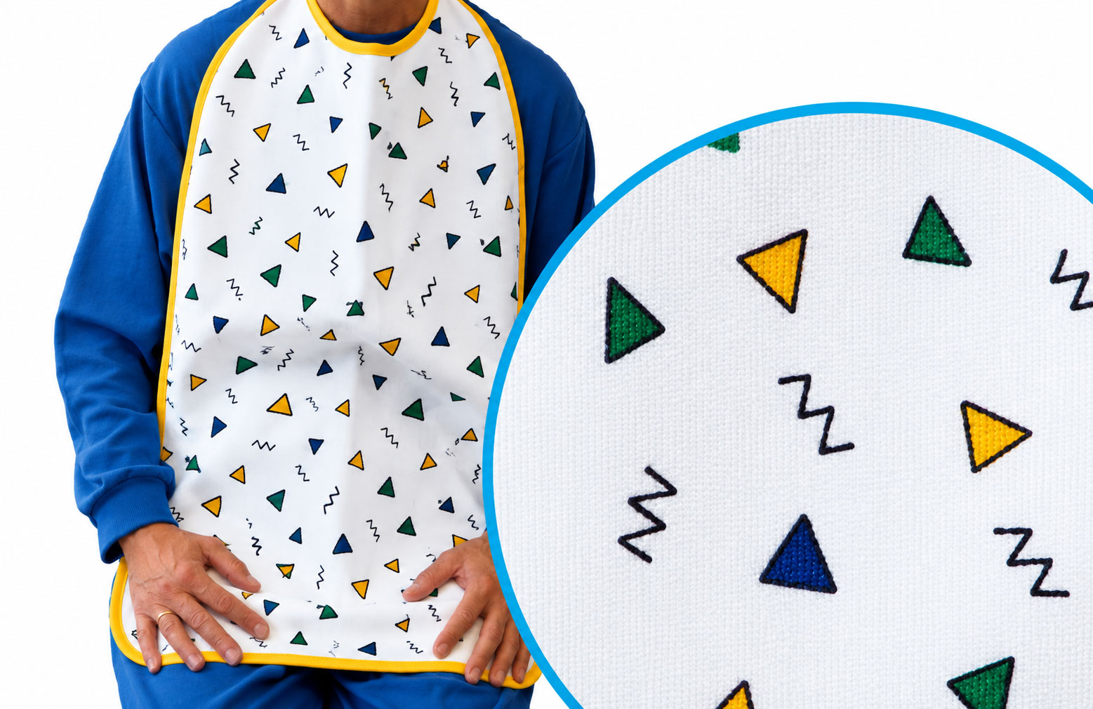 Ein bunten Lätzchen mit geometrischen Mustern in Gelb, Grün und Blau, das von einer Person getragen wird. Die Person hat beide Hände auf dem Lätzchen platziert. Der Hintergrund ist weiß.