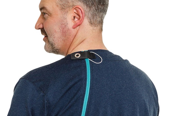 Ein Mann mit kurzen, grauen Haaren trägt ein dunkelblaues Shirt. Am Rücken ist ein Reißverschluss sichtbar, der oben an einem schwarzen Stoffstück befestigt ist, wie eine praktische Halterung oder Öffnung.