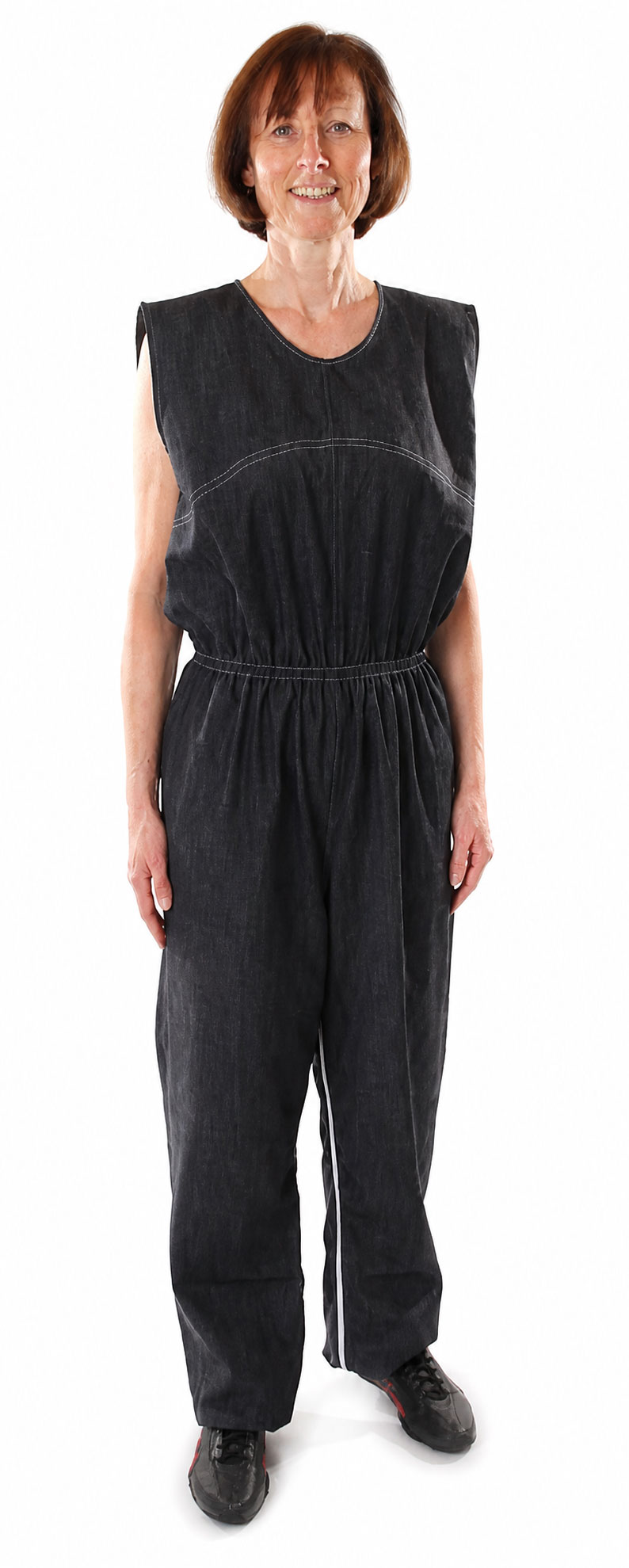 Eine Frau steht in einem grauen, ärmellosen Overall mit elastischem Bund. Der Overall hat eine lockere Passform und ist aus denimähnlichem Material. Der Hintergrund ist weiß.