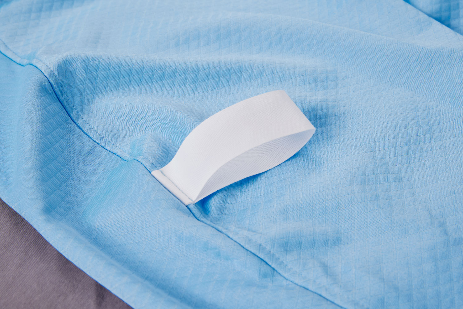 Eine blaue, strukturierte Stoffoberfläche mit einem weißen Befestigungsband. Der Stoff wirkt weich und leicht, der Hintergrund ist grau und neutral.