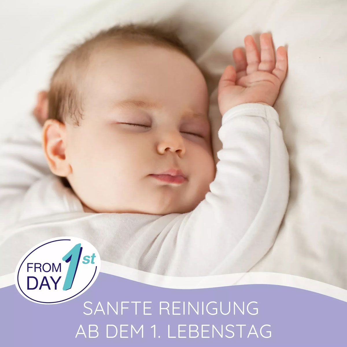 Ein schlafendes Baby mit geschlossenen Augen liegt entspannt auf einem hellen Untergrund. Es trägt einen weißen Schlafanzug, die Hand ist erhoben. Text: -FROM DAY 1st SANFTE REINIGUNG AB DEM 1. LEBENSTAG-.