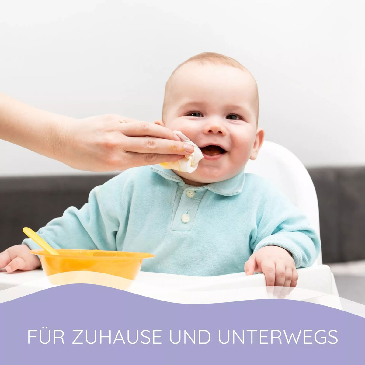 Ein Baby in einem Hochstuhl lächelt, während eine Hand mit einem Tuch seinen Mund abwischt. Vor ihm steht eine gelbe Schüssel mit einem Löffel. Der Hintergrund ist neutral. Text: -FÜR ZUHAUSE UND UNTENWEGS-.