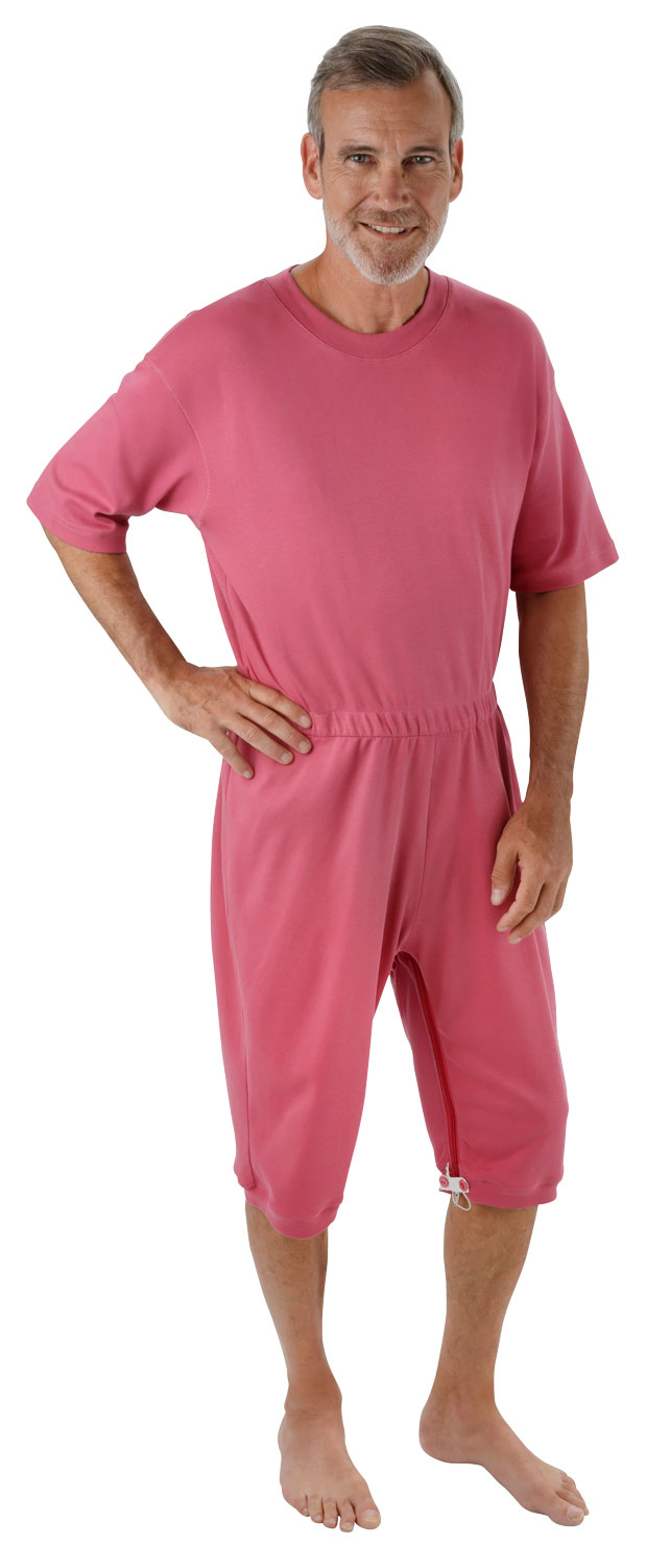 Ein Mann trägt einen rosa Anzug mit kurzen Ärmeln und Hosen, der an der Seite einen Reißverschluss hat. Er steht barfuß und lächelt in die Kamera.