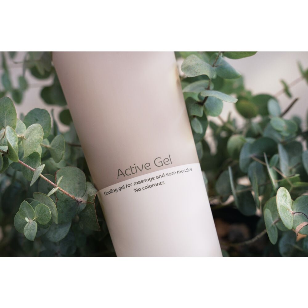 Ein Fläschchen mit der Aufschrift -Active Gel- steht zwischen Eukalyptusblättern. Es handelt sich um kühlendes Gel zur Massage und für muskuläre Beschwerden, ohne Farbstoffe.