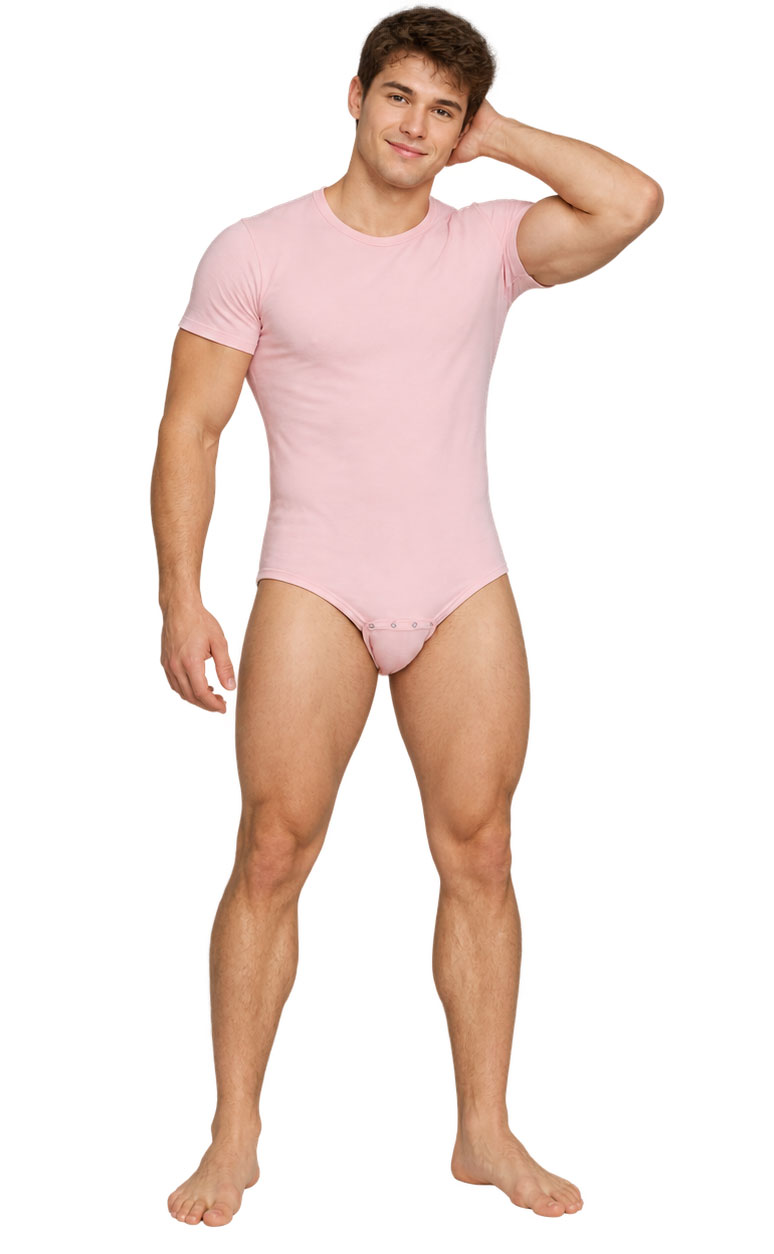 Ein junger Mann mit muskulösem Körper steht lächelnd mit einer Hand hinter dem Kopf. Er trägt ein rosa T-Shirt und einen passenden Bodysuit. Der Hintergrund ist neutral.