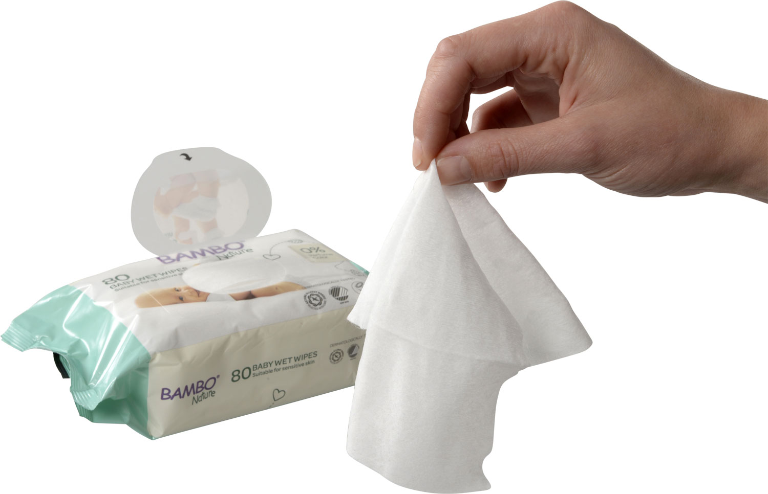 Ein Hand, die ein feuchtes Tuch hält, während eine Packung -BAMBO Nature- Babytücher im Hintergrund sichtbar ist. Die Packung zeigt die Anzahl der Tücher und Hinweise zur Verträglichkeit für empfindliche Haut.