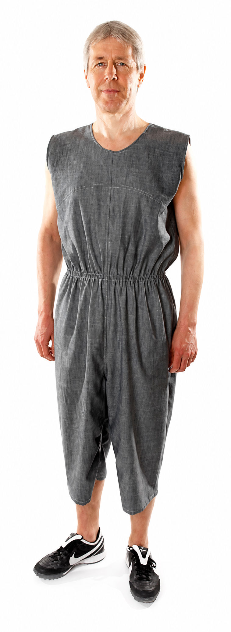 Ein Mann trägt einen grauen, ärmellosen Overall mit elastischem Bund. Er steht aufrecht auf einem weißen Hintergrund und trägt schwarze Sportschuhe.