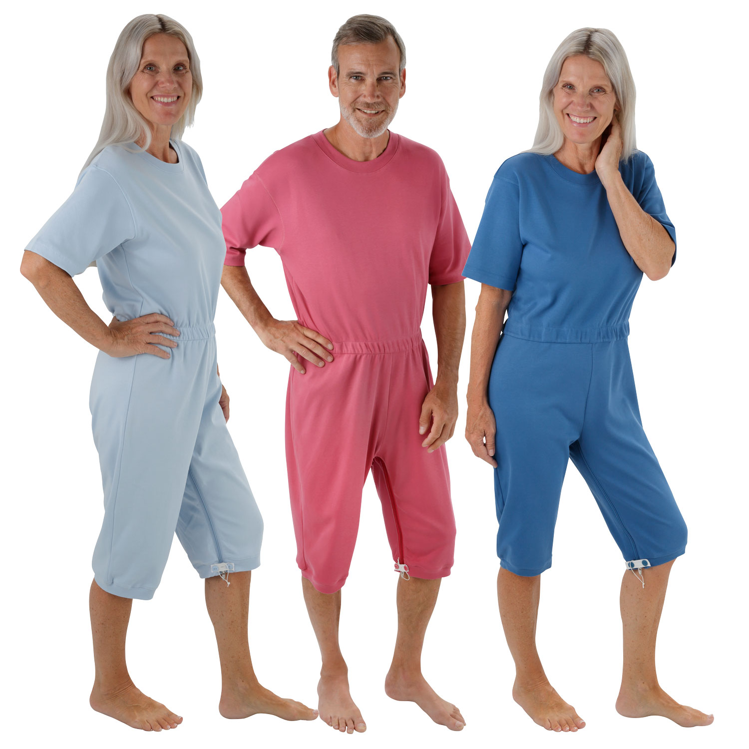 Drei Personen stehen nebeneinander in farbigen Anzügen: einer blauen, einer rosa und einer türkisfarbenen. Alle haben ein lächelndes Gesicht und zeigen ihre Outfits, die medizinischer Natur sein könnten.