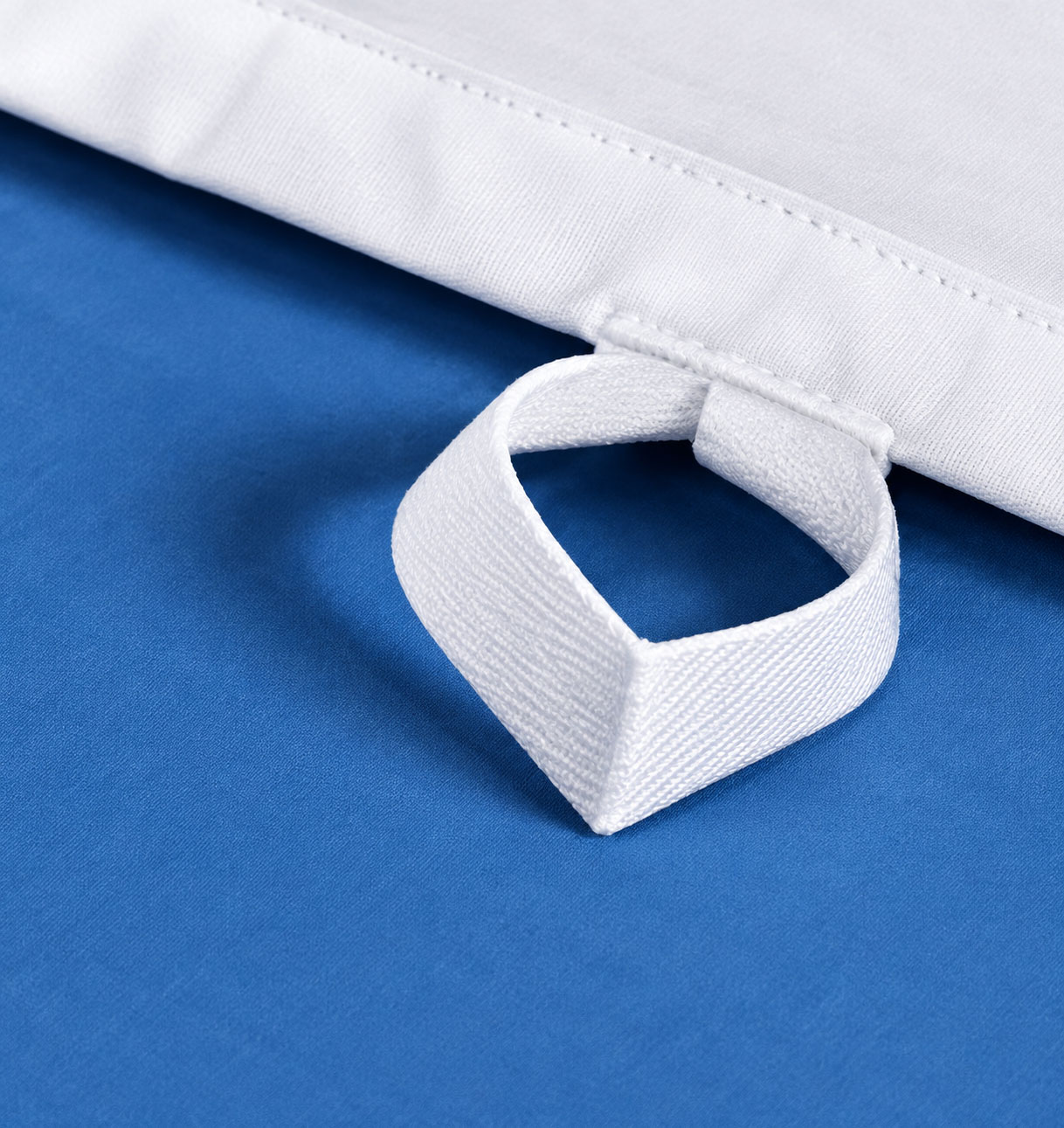 Ein blauer Untergrund zeigt einen weißen Stoff mit einem Schlaufenverschluss. Die Schlaufe ist aus dickem, festem Material und dient zum Sichern oder Aufhängen.
